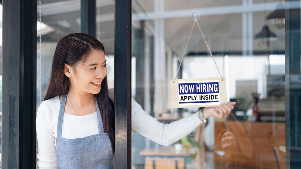 Woman posting sign saying now hiring. 