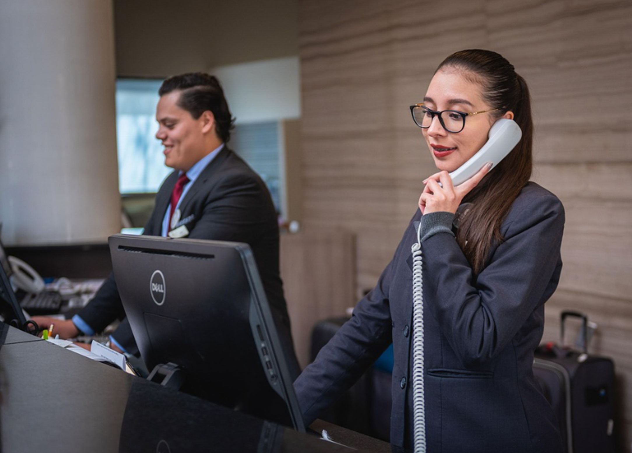 Two people working at a front desk doing customer service. One person is on the phone while using a computer.