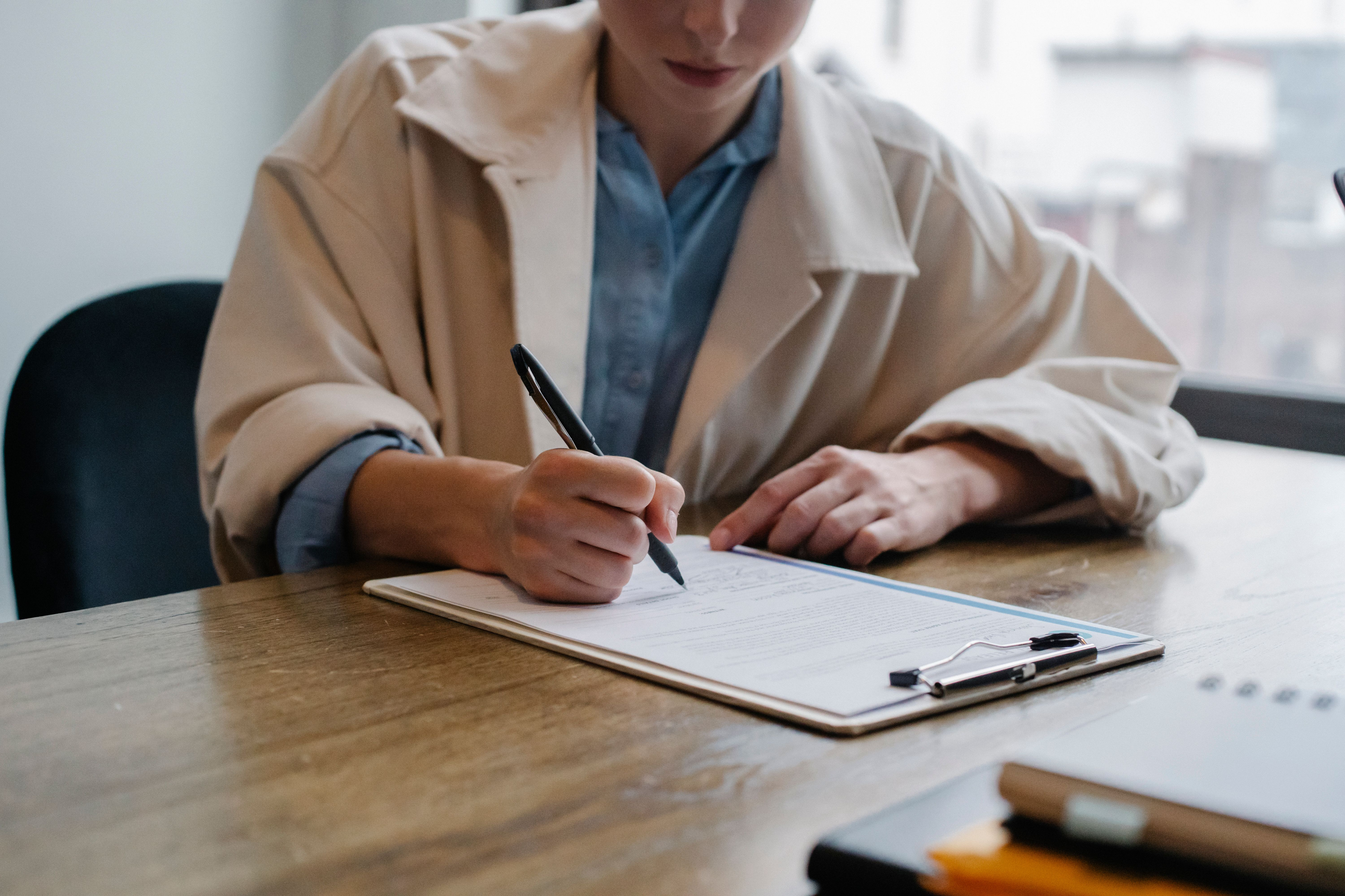 Person holding a pen writing working on resume on a clipboard. 